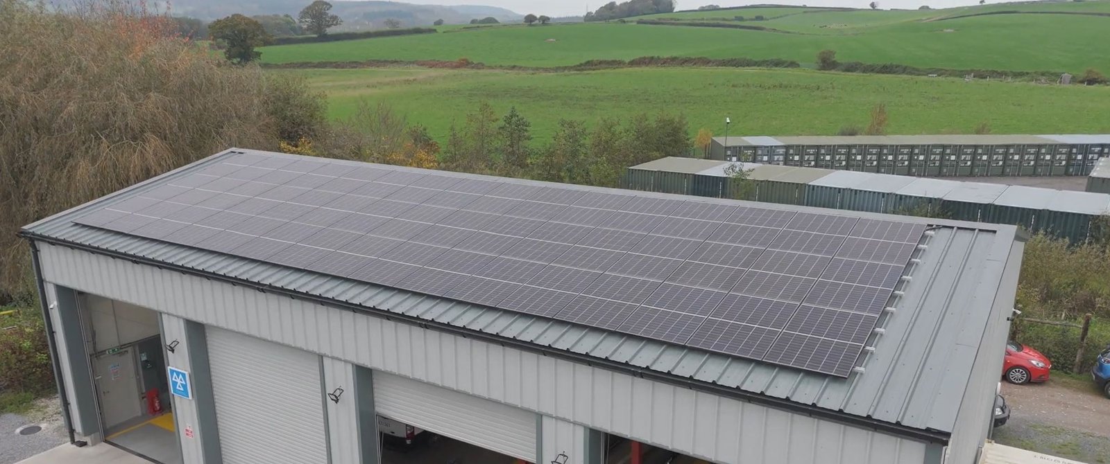 Aerial view of a commercial building roof with solar panels and Devon fields behind