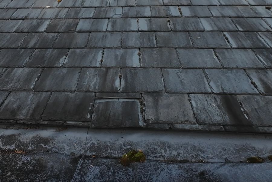 Close-up drone photo of weathered roof slates with a slipped slate and moss in the joints