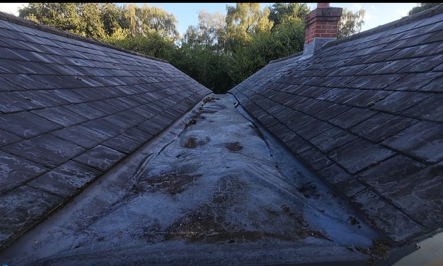 Drone view along a roof valley between two slate pitches, with debris collected in the valley