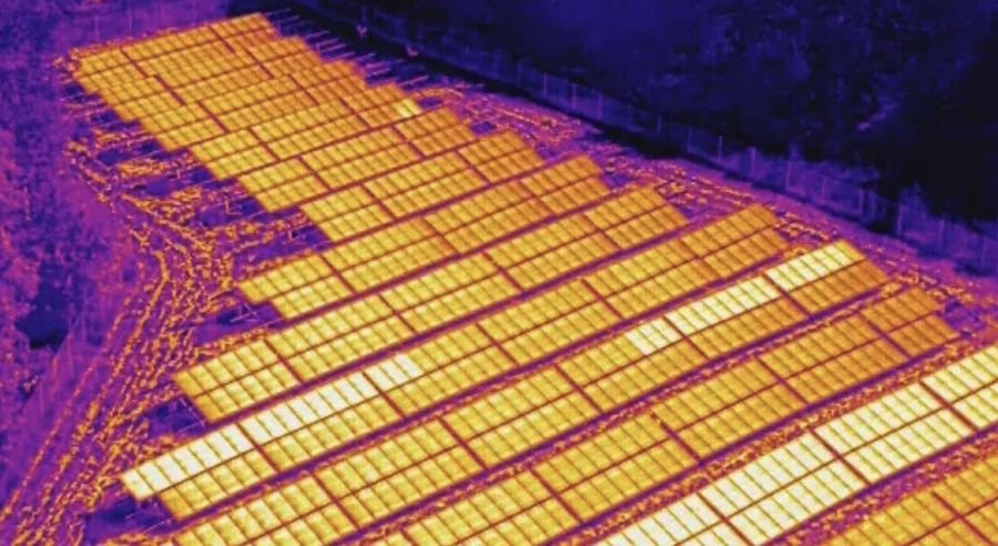 Thermal drone image of rows of solar panels, with warmer panels showing brighter